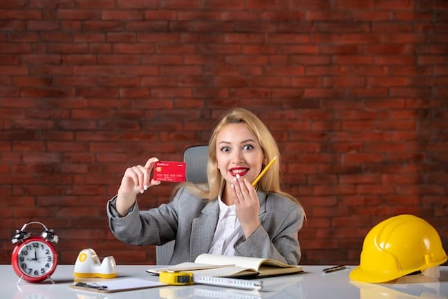 front view Latina engineer sitting behind her working place with red credit card agenda job corporate money contractor builder work business plan