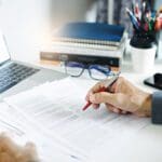 Businessman working on laptop reviewing document reports reading