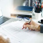 Businessman working on laptop reviewing document reports reading