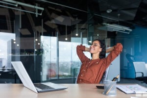 Satisfied happy and successful business woman smiling and resting, hispanic female worker finished work and put her hands behind her head, dreams of victory
