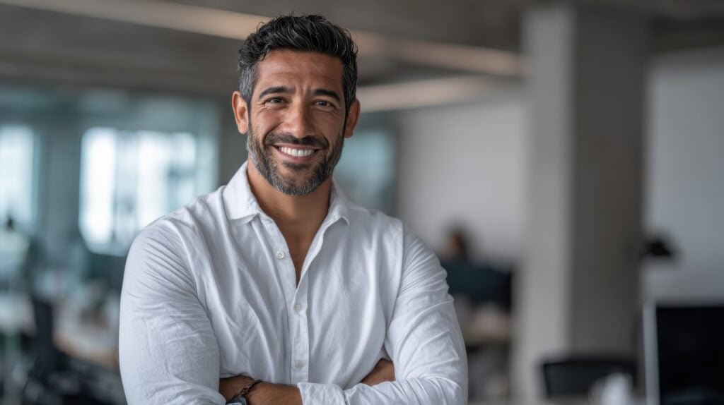 Smiling confident Latin Hispanic businessman CEO standing in modern office looking at camera Middle Eastern professional leader and entrepreneur