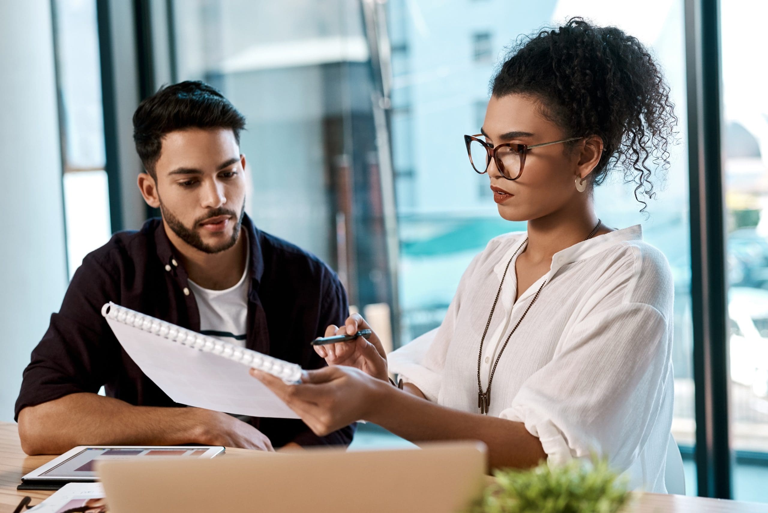 Office, laptop and colleagues with notebook, writing and together for collaboration of project online. Workplace, man and woman with teamwork, graphic designer and digital for photography and editor