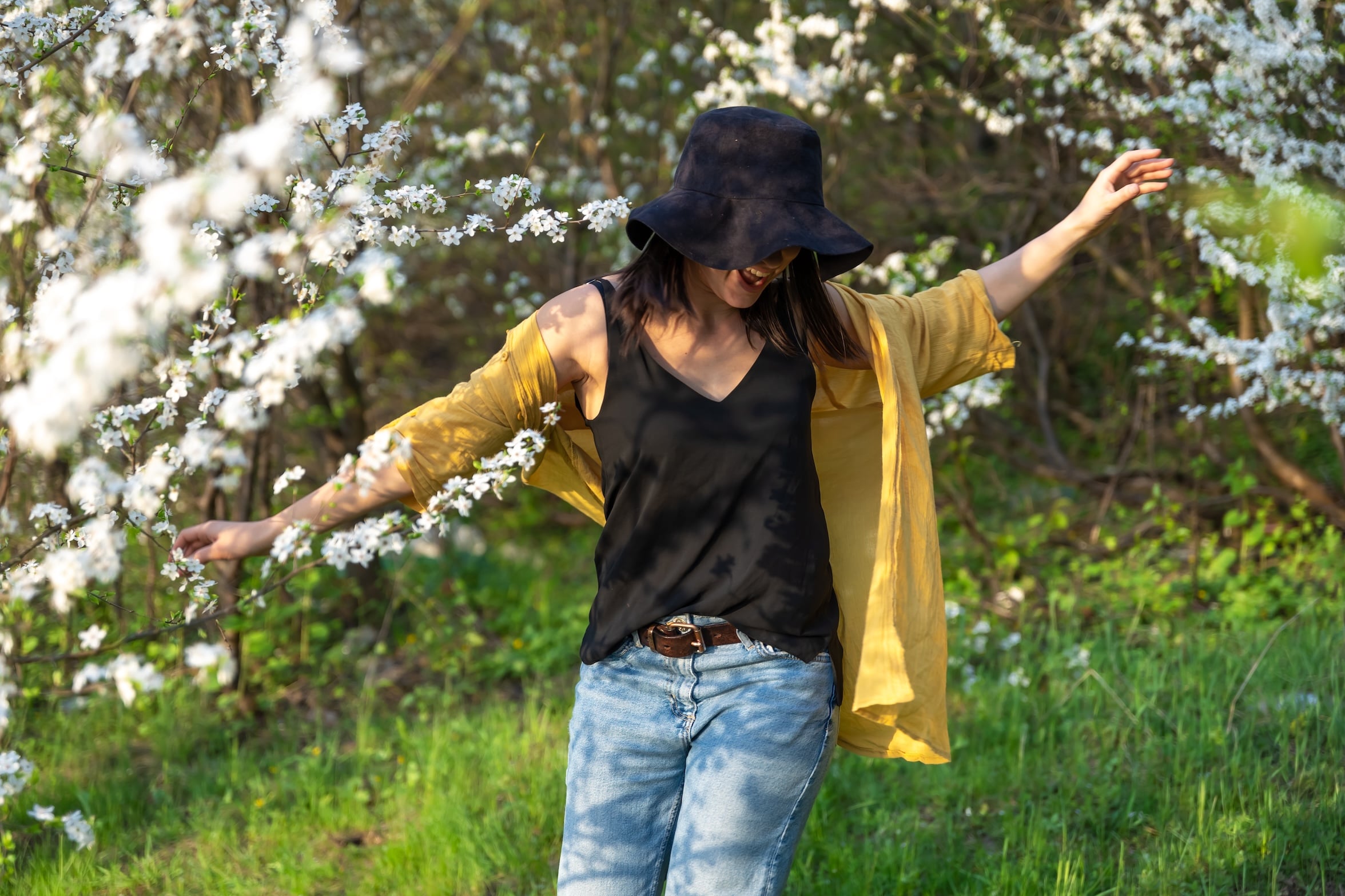 An attractive Latinl in a hat among blooming trees enjoys the smell of spring flowers.