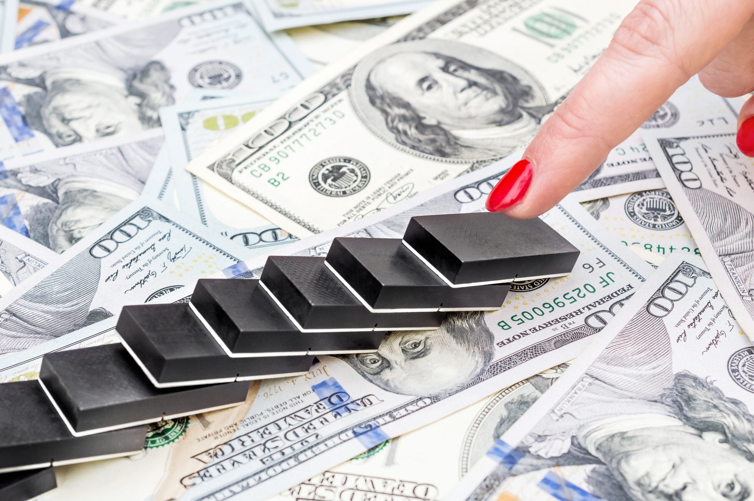 Latina hand pushing domino, making domino effect on dollar backgrounds. Business concept.